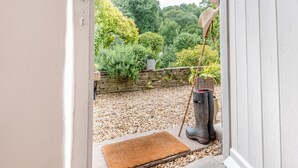 Une porte-fenêtre donnant sur une terrasse en gravier, avec un banc en bois, un pot de fleurs et un mur en pierre.