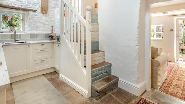 Une cuisine avec des meubles blancs, un escalier en bois et une vue sur la salle à manger.