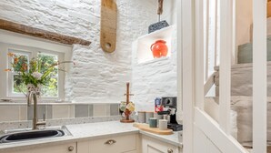 Une cuisine avec un mur en pierre, une fenêtre ornée de fleurs, un évier et une machine à café.