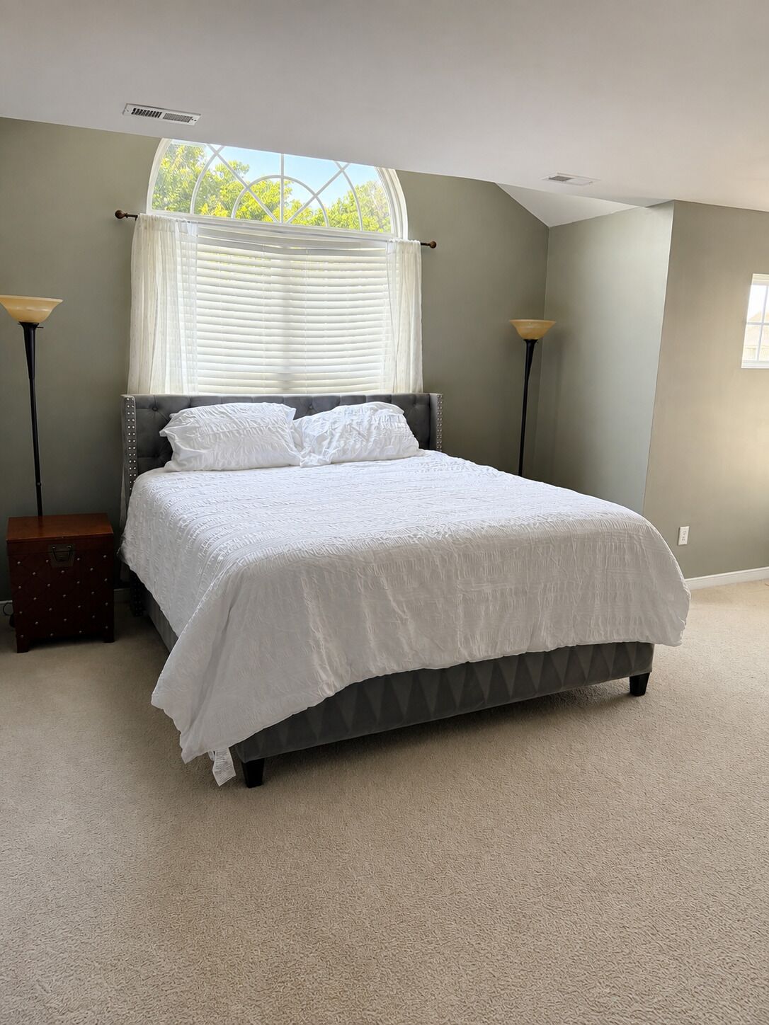 Un dormitorio con cama, ventana con persianas, mesita de noche y lámpara de pie.