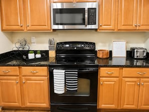 A kitchen with wooden cabinets, a stainless steel microwave, a black stove, and a toaster.