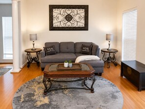 A living room with a grey sofa, two side tables, a coffee table, and a decorative wall piece.