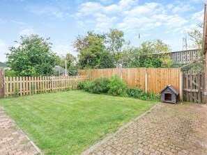 Ein von einer Hecke umgebener Garten mit Rasenfläche, einem Pflasterweg und einem hölzernen Spielhäuschen.