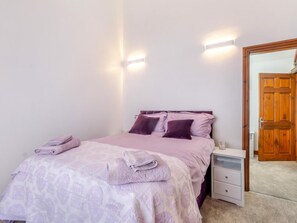 Quarto com cama, almofadas, mesa de cabeceira e criado-mudo.