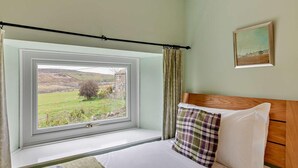 Ein Schlafzimmer mit großem Fenster, einem Bett mit Holz-Kopfteil, einem karierten Kissen und einem Bild an der Wand.
