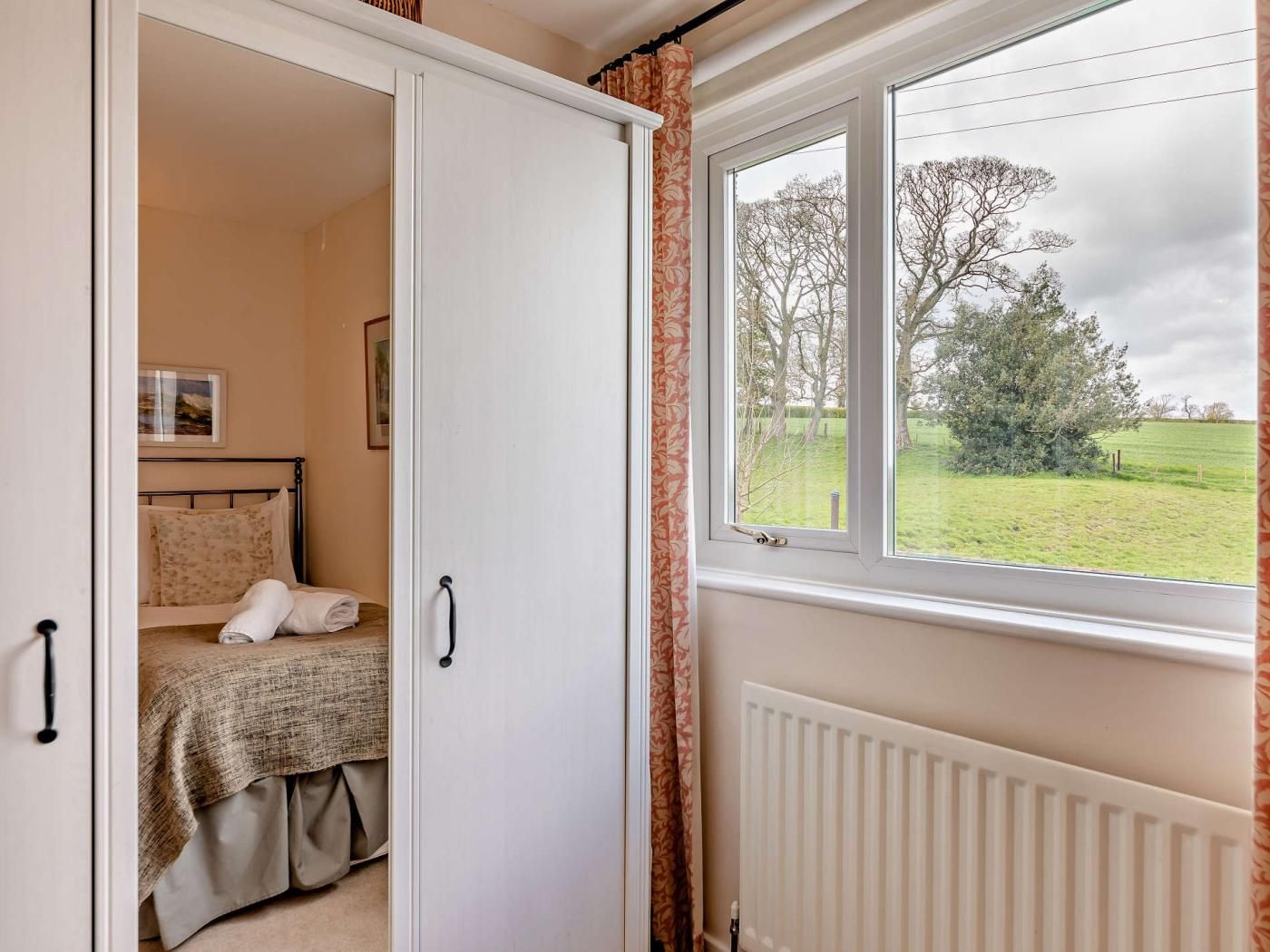 Une chambre à coucher avec un lit, un radiateur et une fenêtre donnant sur un champ verdoyant et des arbres.