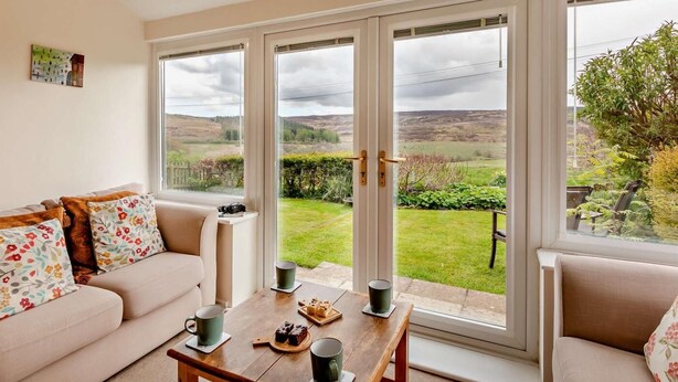 Ein Zimmer mit einer Couch, einem Couchtisch mit Getränken und Snacks sowie großen Fenstern mit Blick auf die Landschaft.
