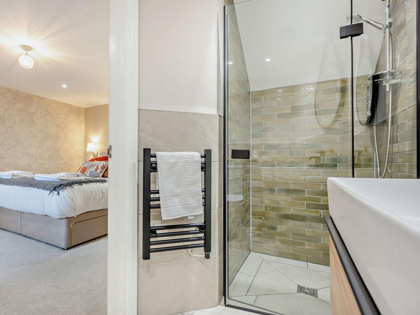 A modern bathroom with a glass shower enclosure, a white sink, and a towel rack.