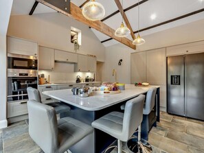 A modern kitchen with a central island, stainless steel appliances, and a high ceiling with exposed beams. - 2 Bed in Cleator (oc-93196) (Ennerdale and Kinniside)