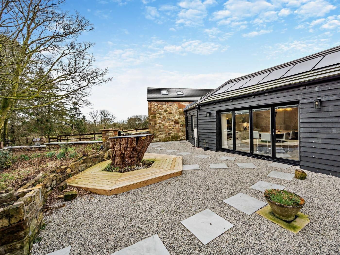 A modern building with a stone wall, a wooden deck, and a large tree stump centerpiece.