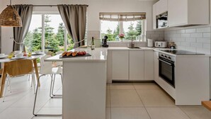 A modern kitchen with a central island, a dining area, and a view of greenery outside. - 2 Bed in Paignton (oc-93062) (Marldon)