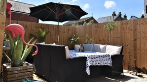 Een terras met een rieten bank, een tafel met een decoratieve tafelkleed en een grote parasol.