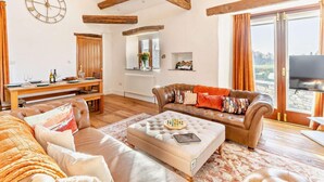 A spacious living area with a wooden ceiling, a dining table set for two, a leather sofa, and a television. - 5 Bed in Broughton-in-furness (oc-93178) (Kirkby Ireleth)