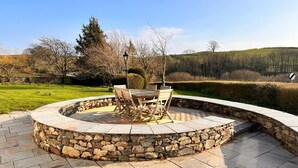 A circular stone patio with a wooden table and chairs, surrounded by a stone wall. - 5 Bed in Broughton-in-furness (oc-93178) (Kirkby Ireleth)