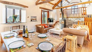 A spacious living area with a high ceiling, wooden beams, a fireplace, and a dining setup. - 5 Bed in Broughton-in-furness (oc-93178) (Kirkby Ireleth)