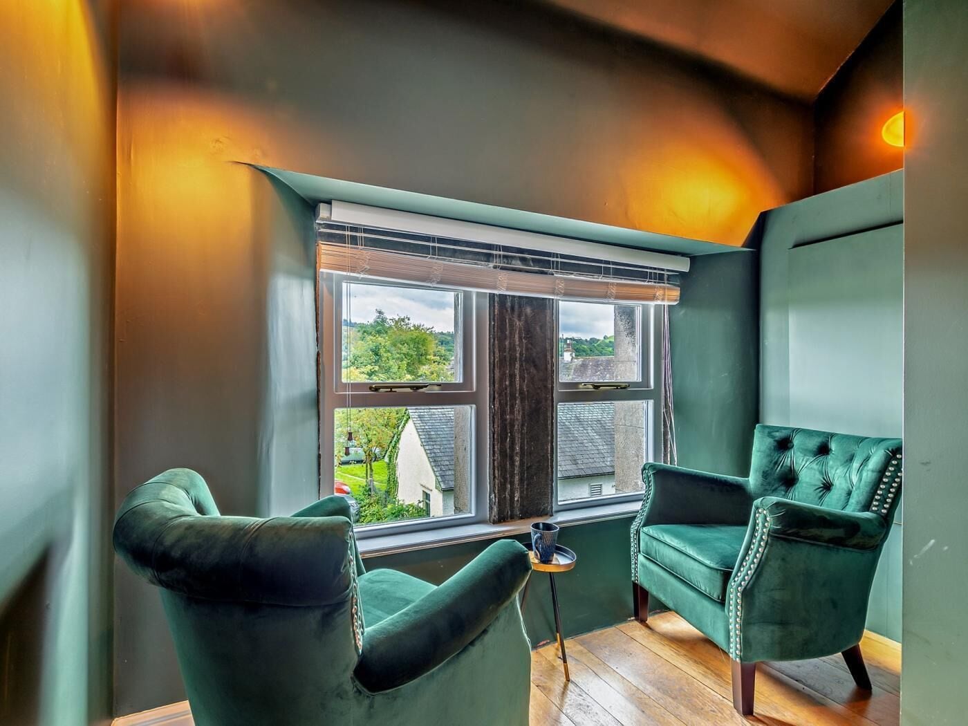A room with a large window, two green armchairs, a small table, and a wooden floor.
