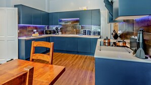 A modern kitchen with dark blue cabinets, a wooden dining table, and a built-in stove. - 2 Bed in Ambleside (oc-93167) (Hawkshead)