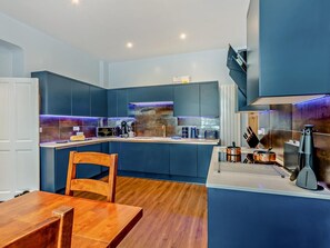 A modern kitchen with dark blue cabinets, a wooden dining table, and a built-in stove. - 2 Bed in Ambleside (oc-93167) (Hawkshead)