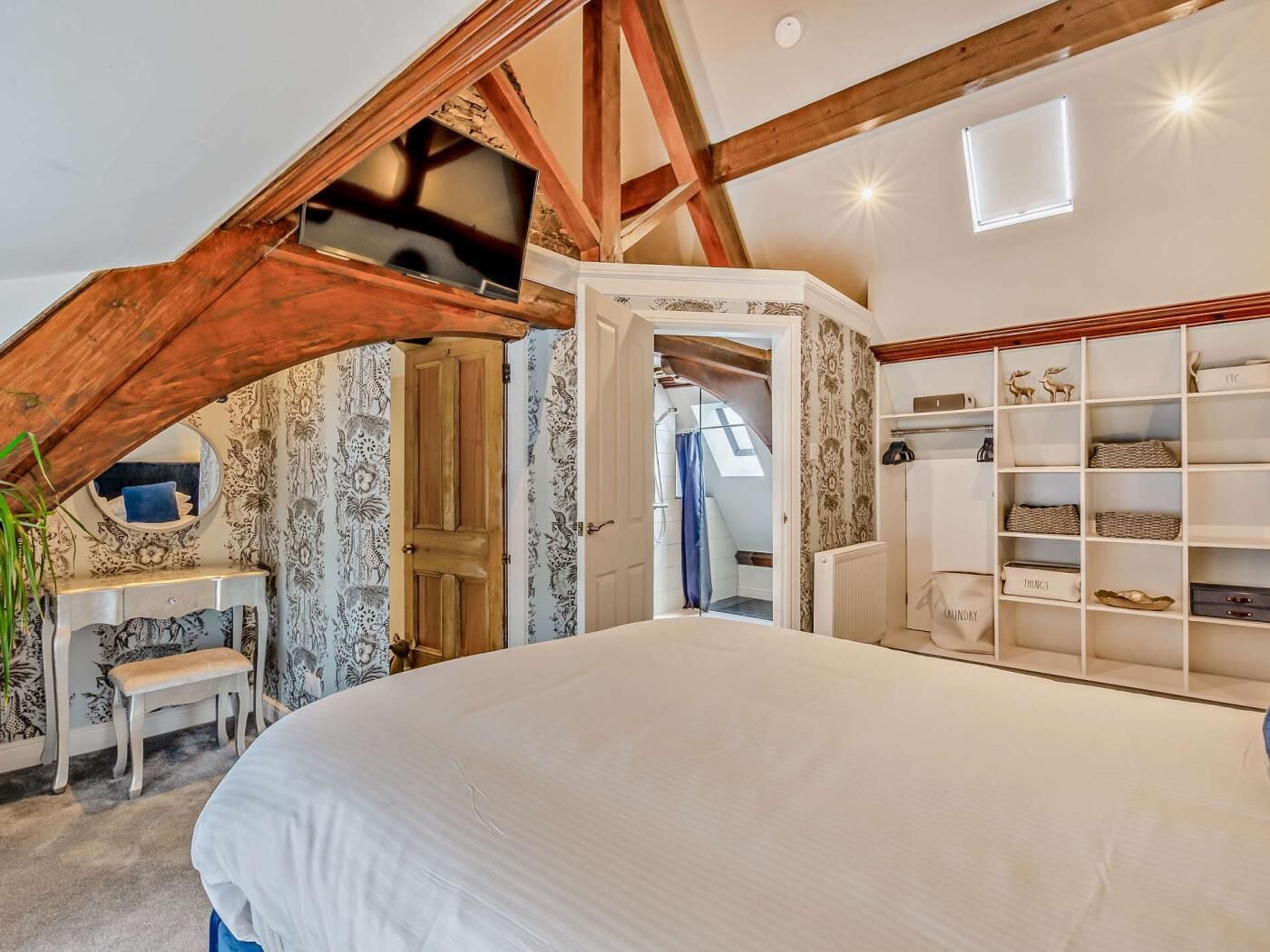 A bedroom with a sloped ceiling, a bed, a vanity, and a wardrobe.