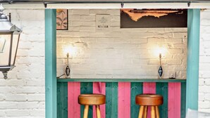 Angolo bar con due sgabelli, una parete in mattoni bianchi e uno scaffale verde acqua con bottiglie.