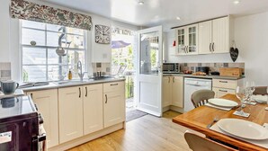 Una cucina moderna con mobili bianchi, un'area pranzo con tavolo in legno e vista tramite una porta in vetro.
