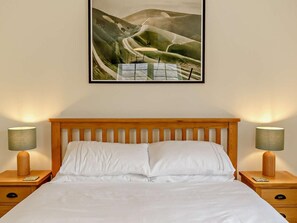 Ein Hotelzimmer mit einem hölzernen Kopfteil, einem Bett mit weißen Bettwäsche, zwei Nachttischen mit Lampen und einem gerahmten Landschaftsbild an der Wand.