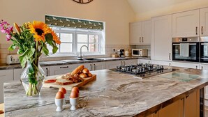 A modern kitchen with a large island, a clock, and a window with a view. - 2 Bed in Harrogate (oc-92721) (Bishop Monkton)