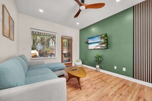 A living room with a sofa, a coffee table, a ceiling fan, a TV, and a green wall. - Walk to Old Town | Family Retreat w/ Big Backyard! (San Diego)