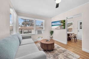 A living room with a sofa, a round coffee table, a painting, and a dining area with chairs and a table. - Walk to Old Town | Family Retreat w/ Big Backyard! (San Diego)