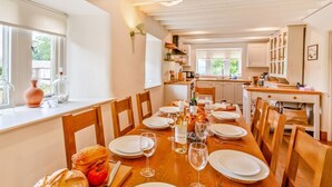 Un espace repas avec une longue table en bois dressée pour le repas, entourée de chaises en bois.