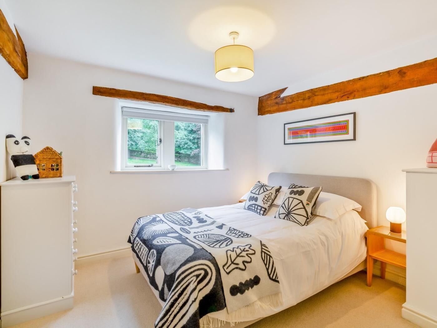Une chambre à coucher avec un lit, une fenêtre, une table de chevet, une lampe et un tableau accroché au mur.