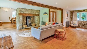 Un salon spacieux avec une cheminée en pierre, un canapé, un coin repas et une vue sur l’extérieur.