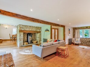 A spacious living room with a stone fireplace, a sofa, a dining area, and a view of the outdoors. - 4 Bed in Skipton (oc-92954) (Cracoe)
