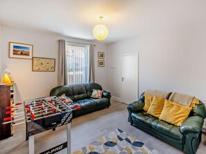 A living room with a foosball table, two leather sofas, a patterned rug, and a window with curtains. - 4 Bed in Cowes (oc-92746) (Cowes)