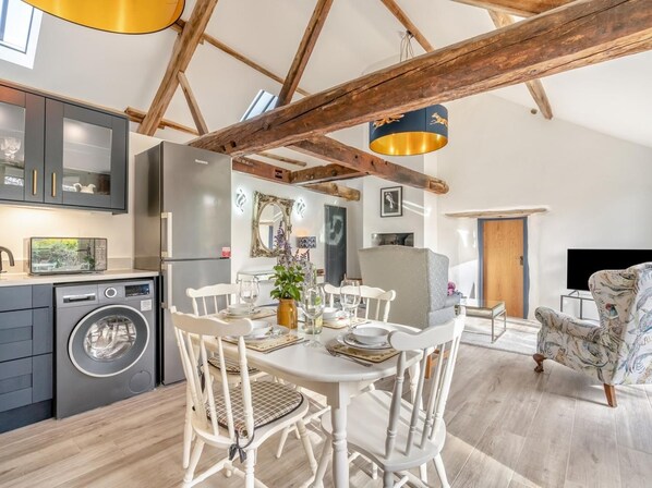 A modern kitchen with a built-in washing machine, a dining area with white chairs, and a large wooden beam ceiling. - 1 Bed in Chop Gate (oc-93101) (Chop Gate)