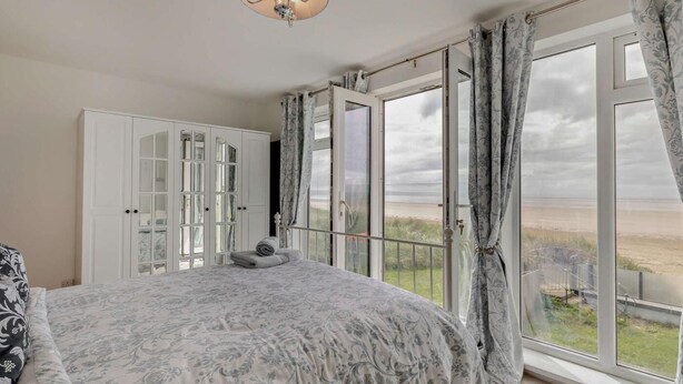 A bedroom with a bed, a wardrobe, a balcony with a view of the beach, and a hanging light fixture. - 3 Bed in Burnham-on-sea (oc-92964) (Brean)