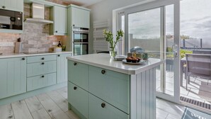 A modern kitchen with light green cabinets, a central island, and a view to the outside. - 3 Bed in Burnham-on-sea (oc-92964) (Brean)