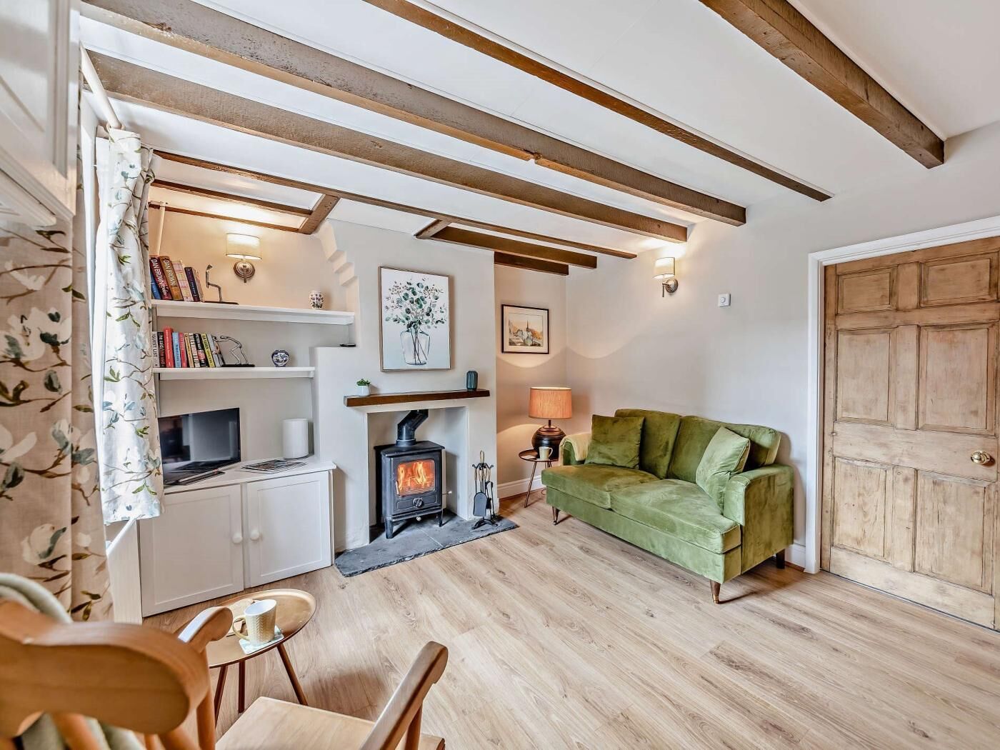 Un salón acogedor con chimenea, un sofá verde, vigas de madera y una estantería.