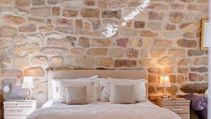 A bedroom with a stone wall, a bed with multiple pillows, two bedside tables with lamps, and a nightstand with a lamp. - 2 Bed in Chop Gate (oc-93098) (Chop Gate)