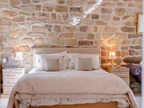 Ein Schlafzimmer mit Steinwand, einem Bett mit vielen Kissen, zwei Nachttischen mit Lampen und einem Beistelltisch mit einer Lampe.