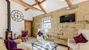A cozy living room with a stone wall, a fireplace, a large clock, and a television. - 2 Bed in Chop Gate (oc-93098) (Chop Gate)