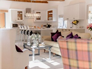 Ein modernes Wohnzimmer mit einem Glastisch, einer Couch mit Kissen und einem Essbereich mit Stühlen und einer Chandelier.
