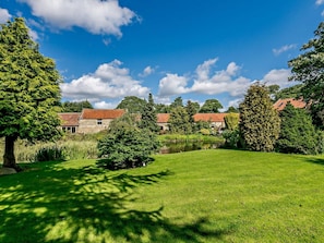 A grassy area with a pond, trees, and stone buildings with red roofs. - 1 Bed in Chop Gate (oc-93100) (Chop Gate)