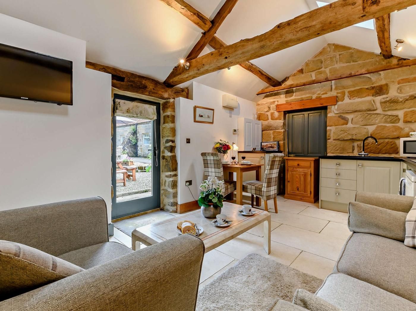 A cozy living room with a stone wall, wooden beams, a flat-screen TV, and a dining area with a table and chairs.