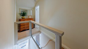 A modern interior with a glass railing, a wooden dresser, and a mirror reflecting a plant and a door. - 1 Bed in Machynlleth (oc-92689) (Pennal)