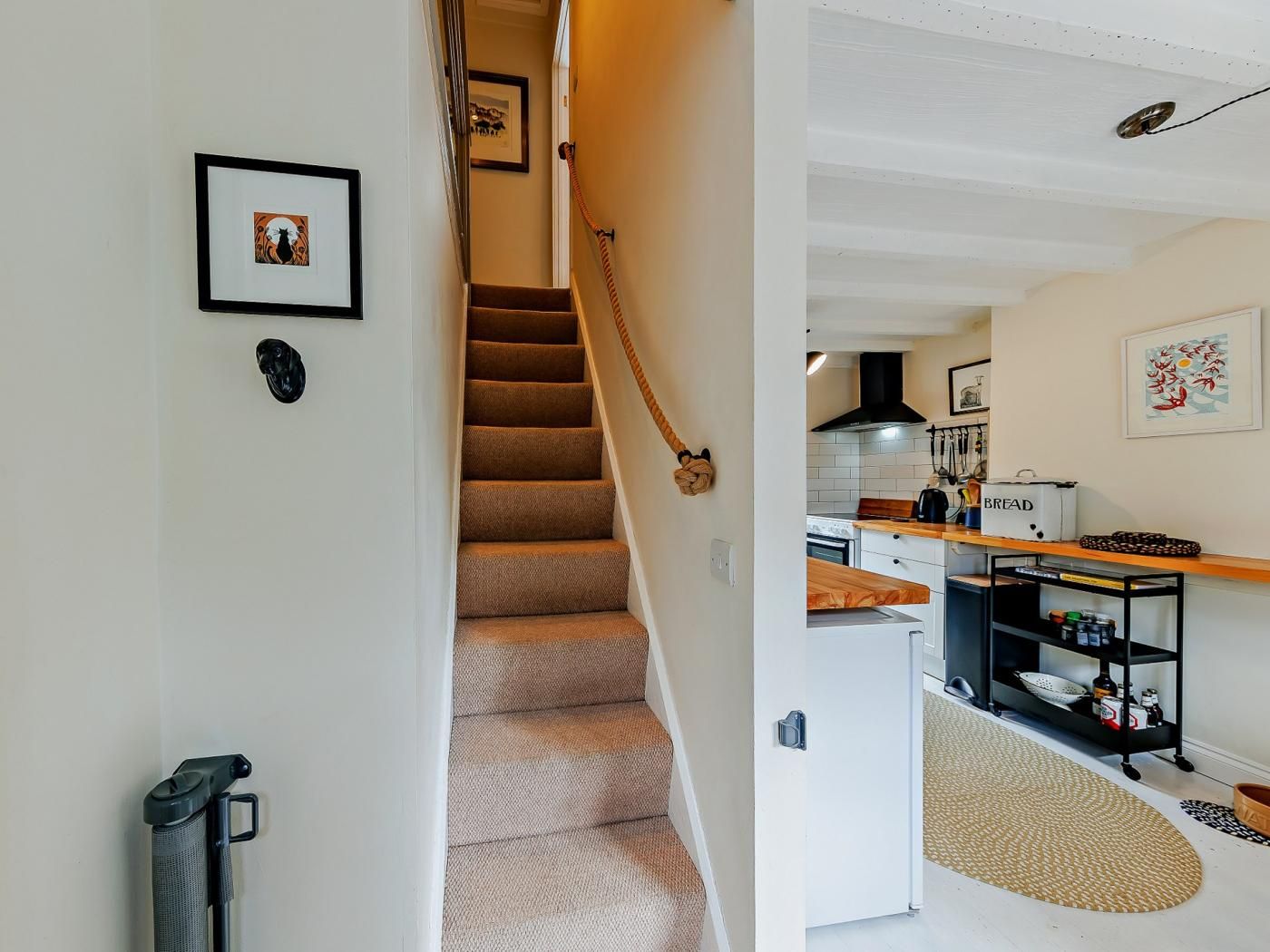 A staircase leading to a kitchen with a bread box, a hanging rack, and a patterned rug.