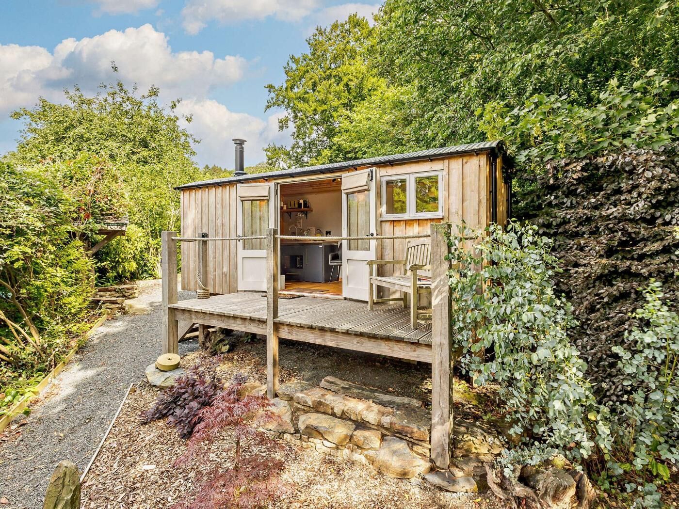 A wooden cabin with a deck, a chimney, and a small kitchen area.