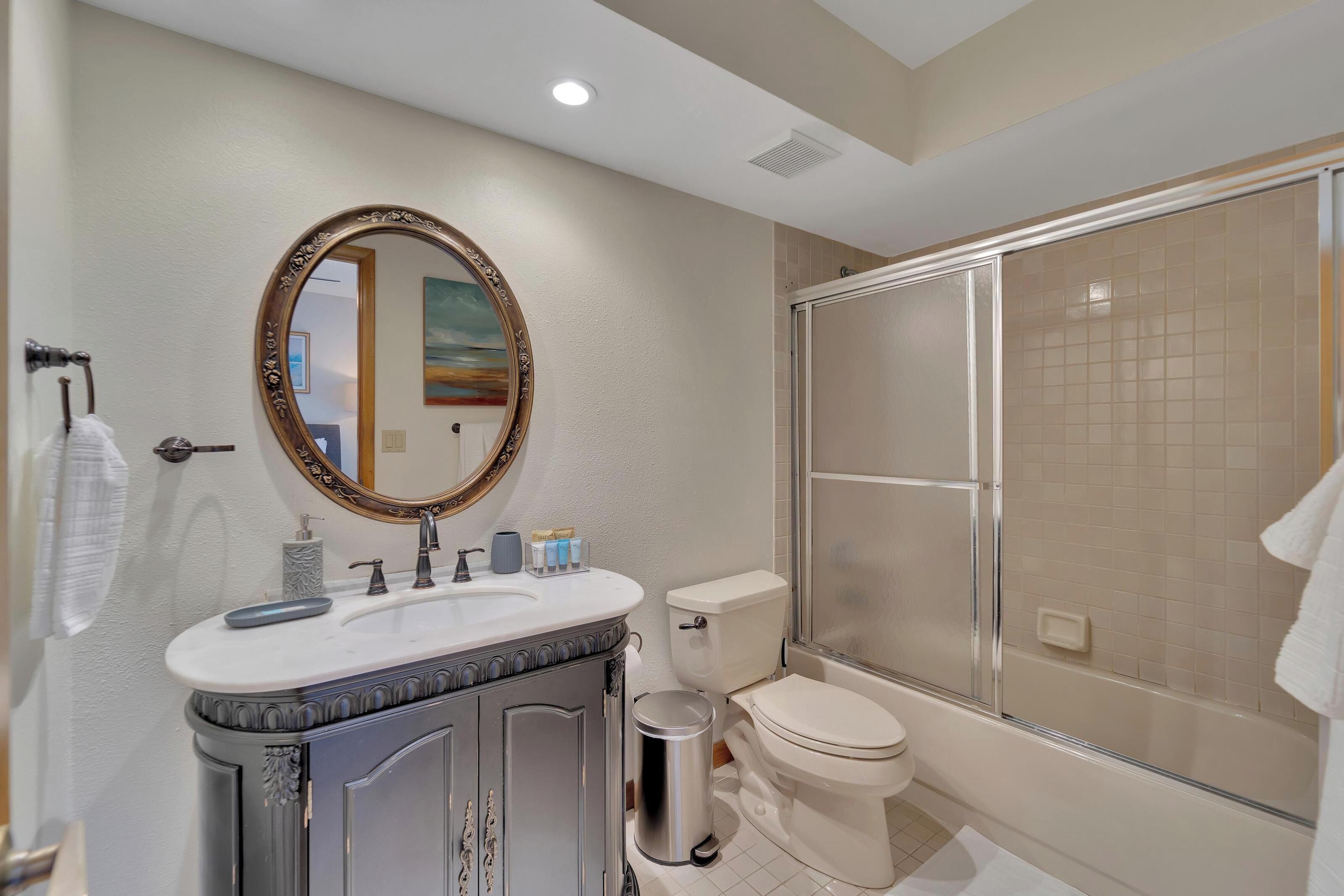 A bathroom with a large mirror, a sink, a toilet, and a glass-enclosed shower.