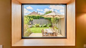 Ein Oberlichtfenster mit Blick auf eine Hinterhof-Terrasse, inklusive Esstisch und einem großen Sonnenschirm.