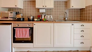Een keuken met witte kastjes, een magnetron, een fornuis en een spoelbak.